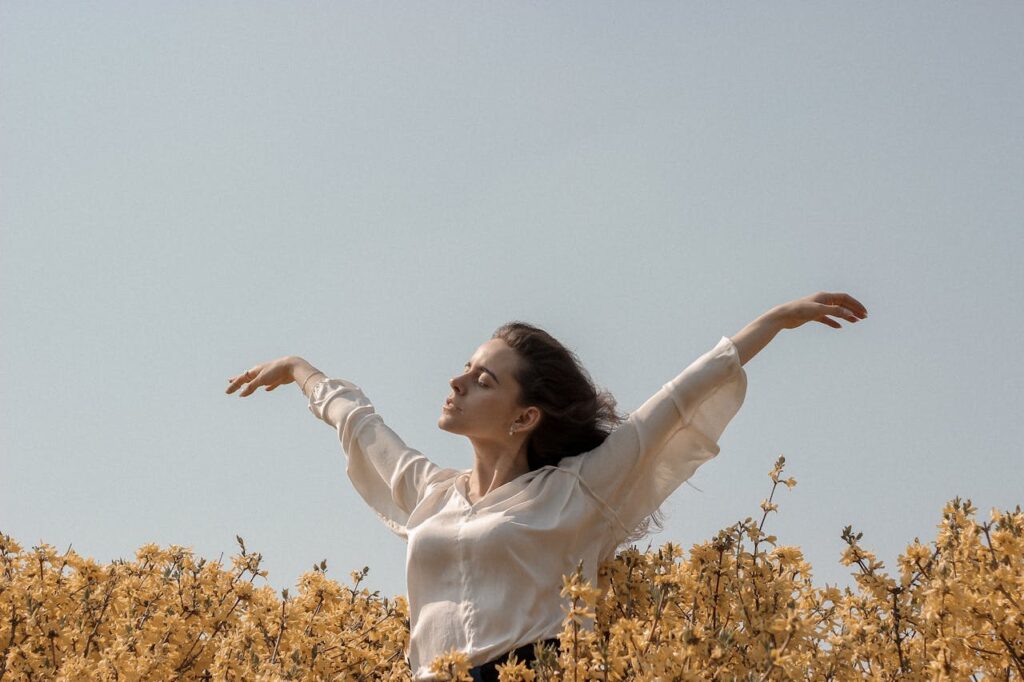 Woman with arms raised in a sunny field of yellow flowers, capturing freedom and serenity.